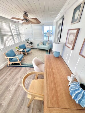 A modern living room with a wooden dining table, blue chairs, a light blue sofa, and a ceiling fan. - NEW! The Oasis on Primo! Next To Margaritaville & In The Heart of Time Square! (Fort Myers Beach)