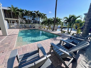 A swimming pool with lounge chairs and palm trees. - NEW! The Oasis on Primo! Next To Margaritaville & In The Heart of Time Square! (Fort Myers Beach)