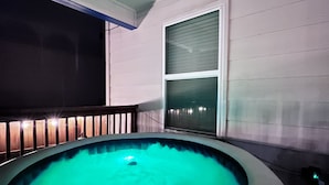 A hot tub with a teal-colored water feature, surrounded by a wooden deck and a white wall.