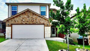 A two-story house with a stone facade, a garage, and a well-maintained lawn with a tree.