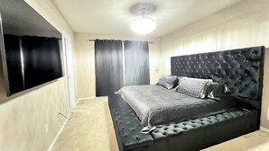 A bedroom with a large bed, a flat-screen TV, and a ceiling fan.