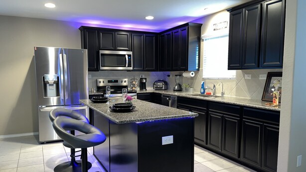 A modern kitchen with dark cabinetry, stainless steel appliances, a granite countertop island, and a bar stool.