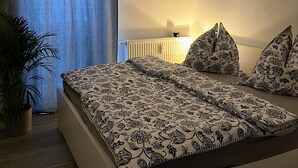 Ein Schlafzimmer mit einem Bett, einer Topfpflanze, einem Heizkörper und einer Pendelleuchte.