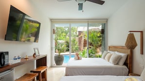 A hotel room with a bed, a desk with a computer, a TV, and a view of a swimming pool and greenery.