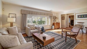 Un salón amplio con un gran ventanal, un sofá, una mesa de centro y una silla de madera.