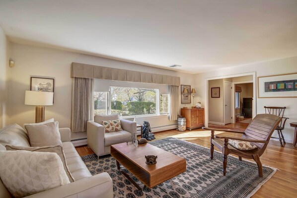 Un salón amplio con un ventanal grande, un sofá, una mesa de centro y una silla de madera.