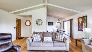 Uma sala de estar com um sofá cinzento, uma poltrona de couro castanho, piso de madeira, uma porta de madeira, um relógio e um candelabro.