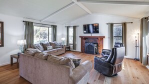 Uma sala de estar ampla com lareira, um sofá, uma poltrona reclinável e uma TV fixada na parede.