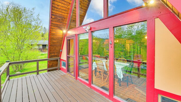 A wooden deck with a glass enclosure, a red exterior, and a view of a patio with tables and chairs. - Walk to Ski Lift! Charming Hunter A-Frame (Lanesville)