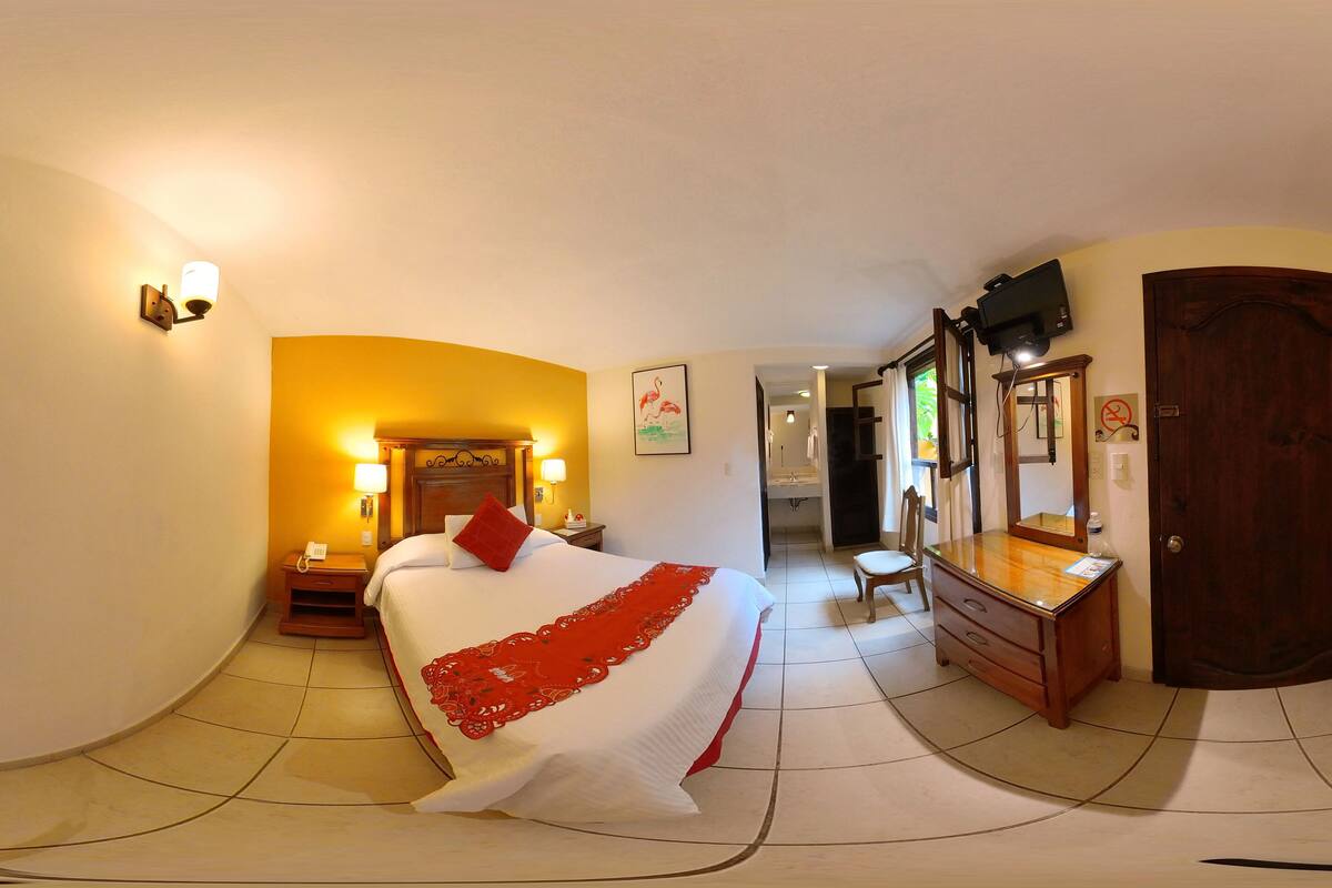 Una habitación de hotel con cama, mesitas de noche, cómoda, espejo y puerta.