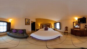 Una habitación amplia con una cama grande, un sofá, un tocador con espejo y un televisor.
