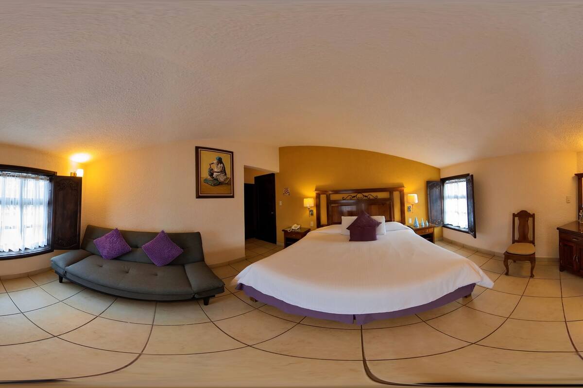 Una habitación amplia con una cama grande, un sofá, un tocador con espejo y un televisor.