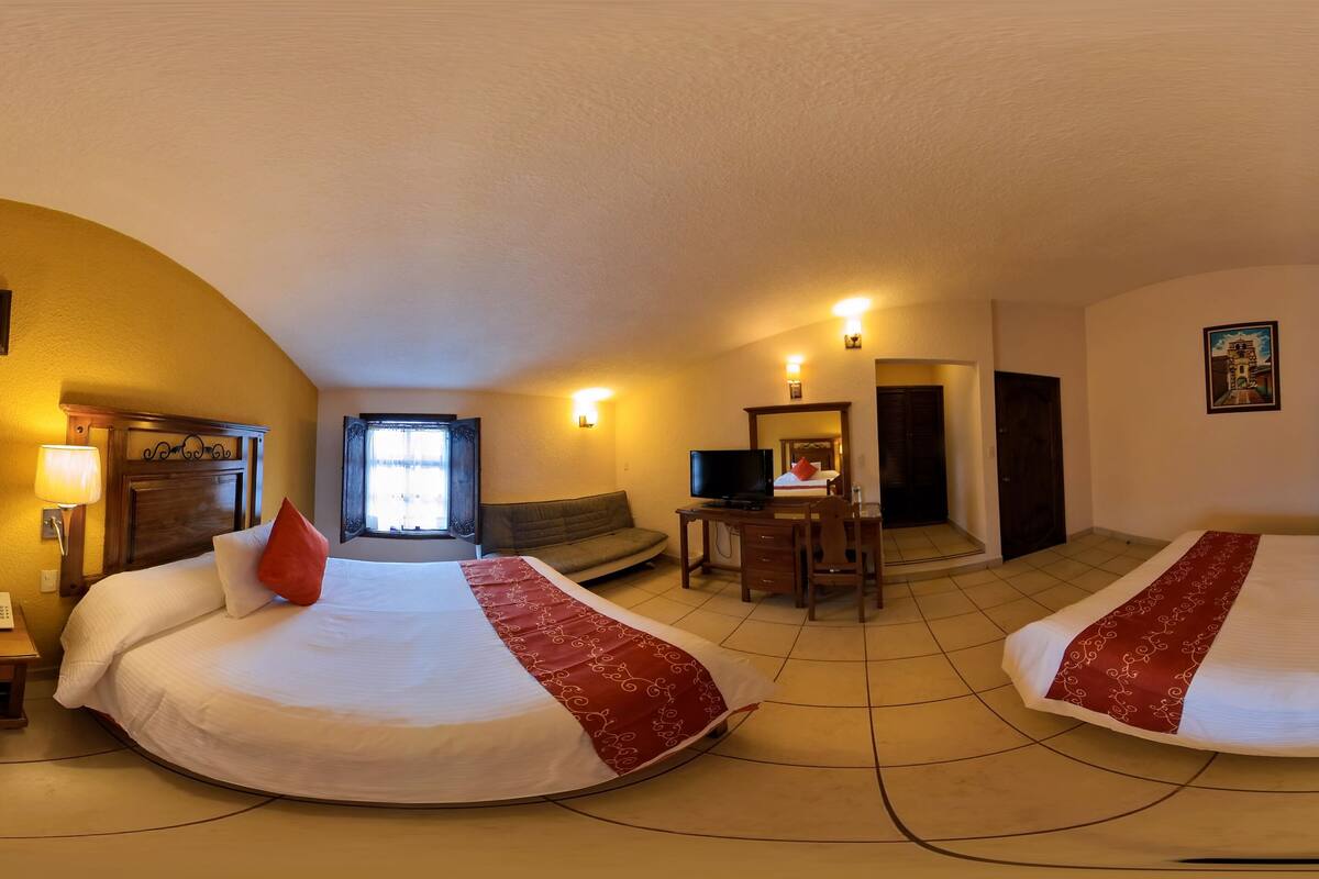 Habitación de hotel con dos camas, un escritorio, televisor y sofá.