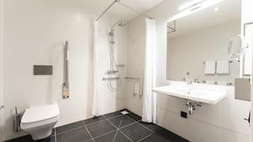 Une salle de bain moderne avec des toilettes blanches, une douche équipée d’un pommeau de douche à main, un lavabo avec un miroir et des murs carrelés.