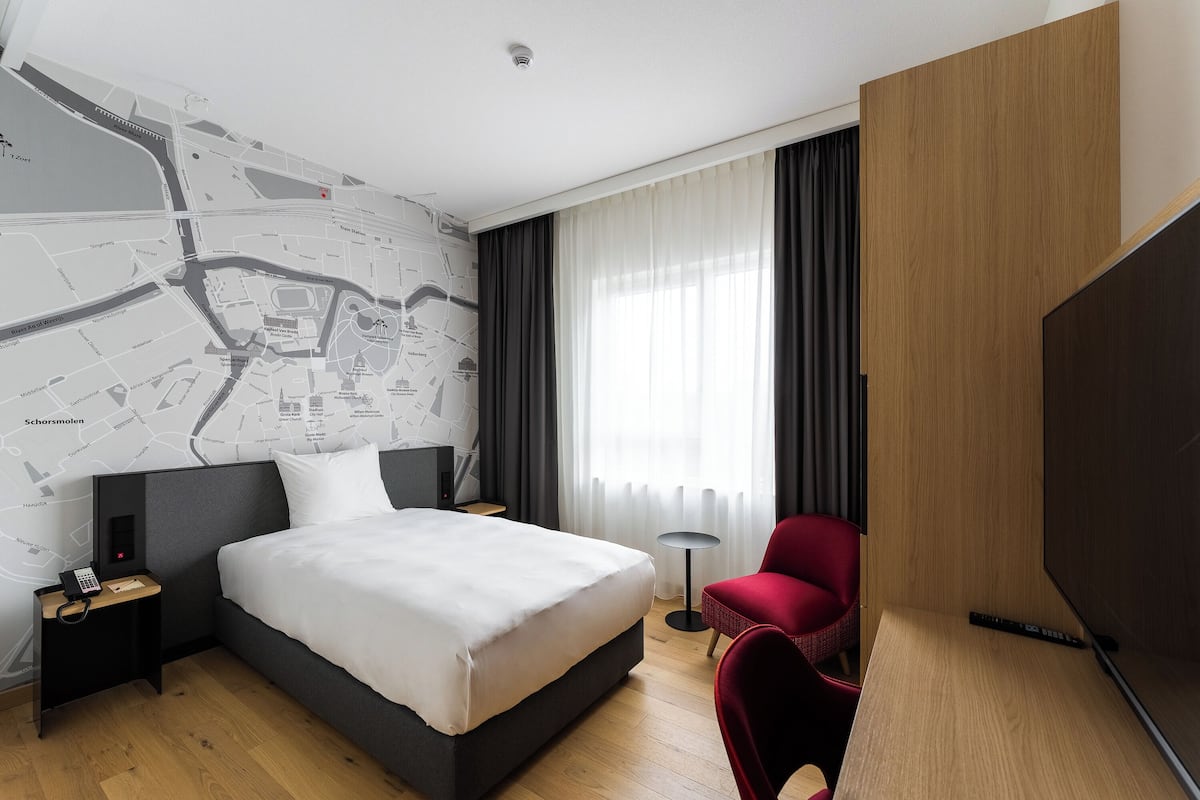 A modern hotel room with a large bed, a red chair, a TV, and a map on the wall.
