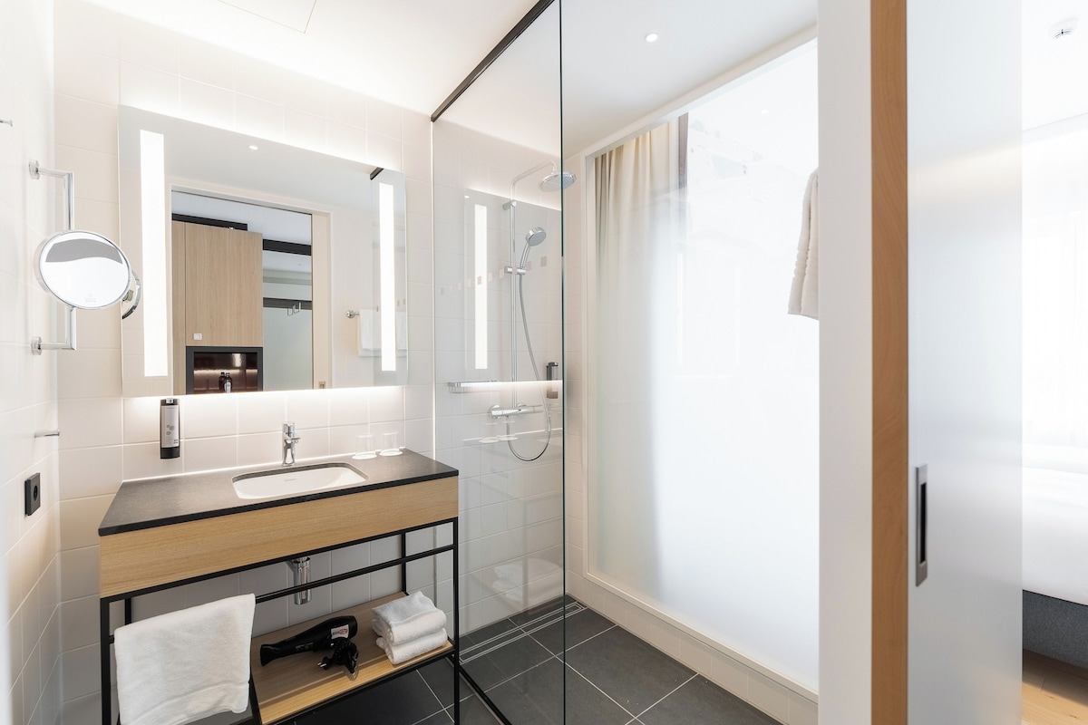 A modern bathroom with a glass shower enclosure, a wooden vanity, and a large mirror.
