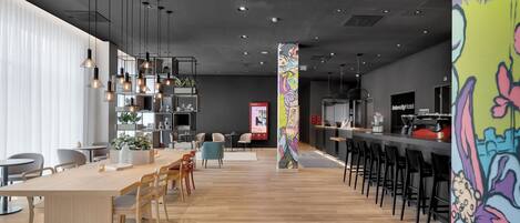 Un restaurante moderno con una larga mesa de madera, taburetes negros y lámparas colgantes.