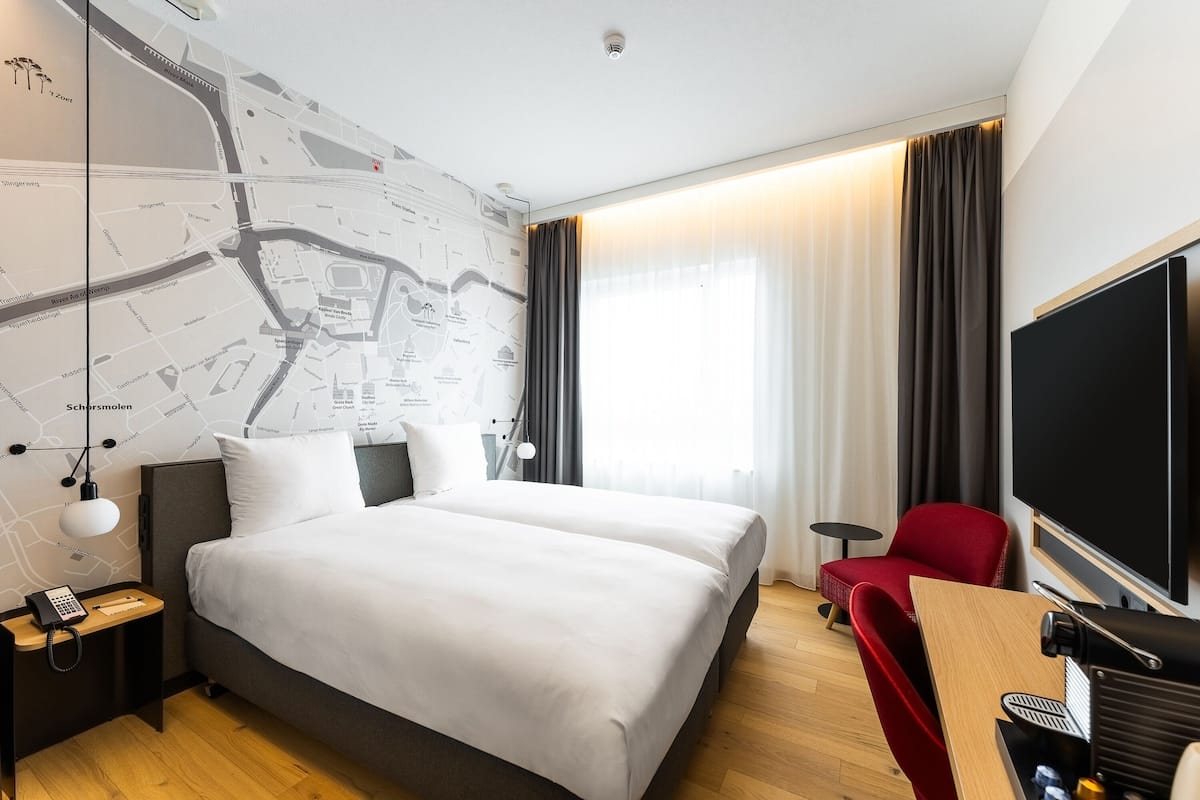 A modern hotel room with a large bed, a desk with a chair, a flat-screen TV, and a map on the wall.