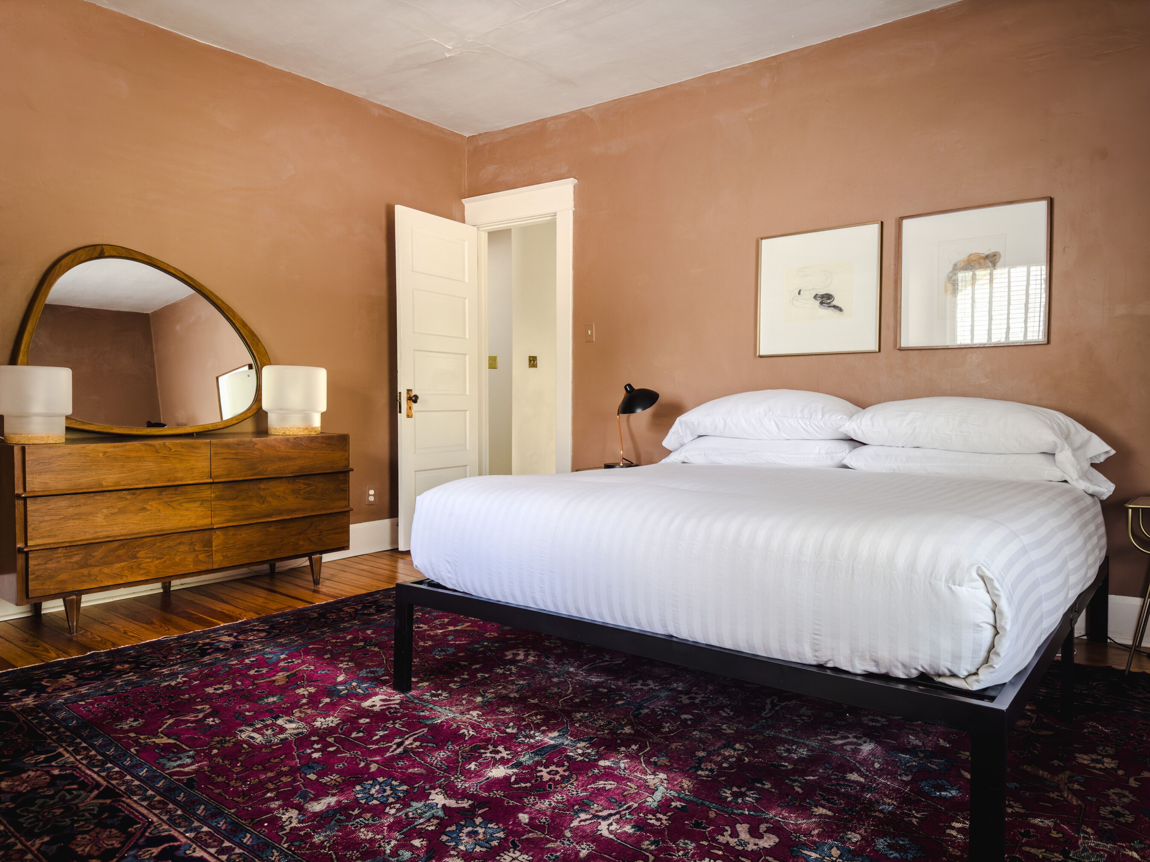 A bedroom with a bed, a dresser, a mirror, and a door.