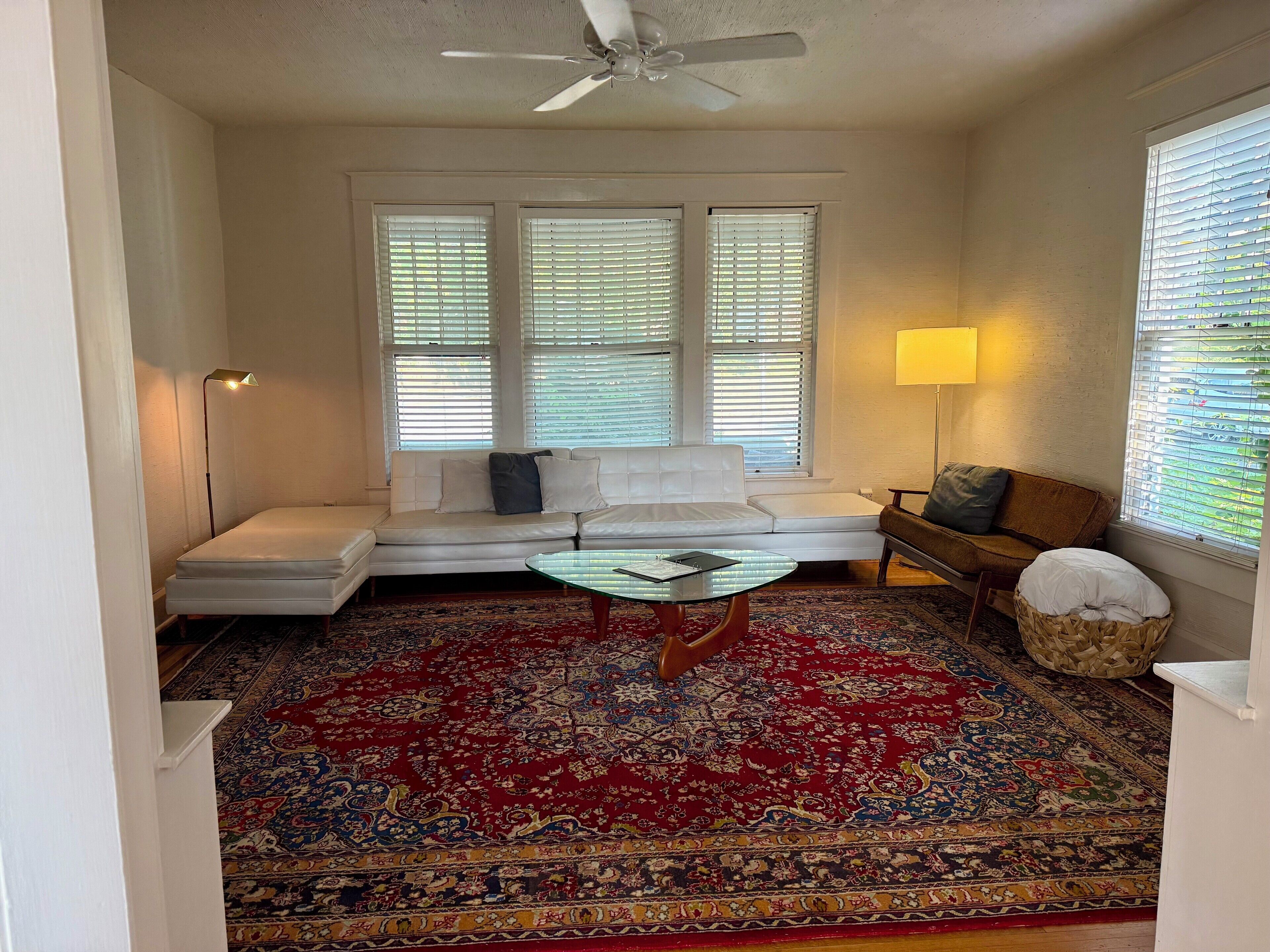 Un salon avec un canapé blanc, une table basse en verre, un tapis à motifs et un ventilateur de plafond.