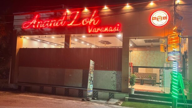 Ein Gebäude mit einem Neonlichtschild mit der Aufschrift 'Anand Loh Varanasi' und einem Schild, das 'zimmer mit und ohne Klimaanlage' anzeigt.