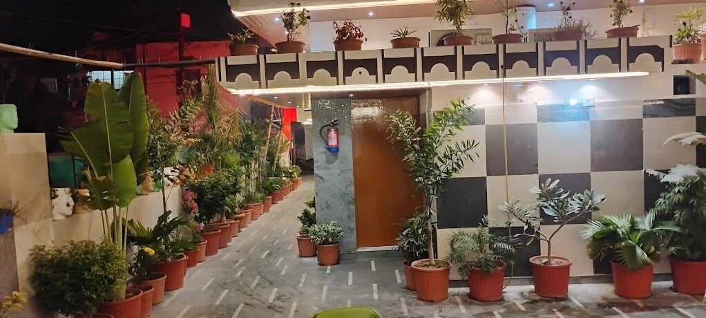 A hotel corridor with potted plants lining the walls and a checkered floor pattern.