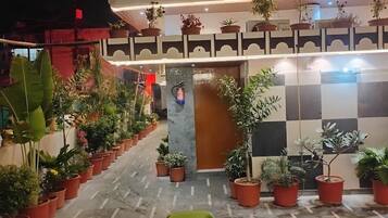 A hotel corridor with potted plants lining the walls and a checkered floor pattern.