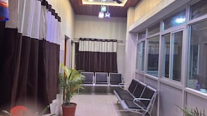 A waiting area with a row of chairs, a potted plant, and a window with blinds. - ANAND LOK VARANASI  (Varanasi)