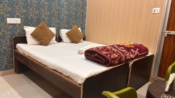 A single bed with a white mattress, two pillows, a maroon blanket, and a green chair.