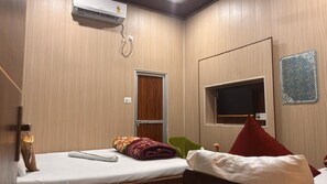 Ett hotellrum med en säng, en tv, en dörr och en luftkonditioneringsanläggning.