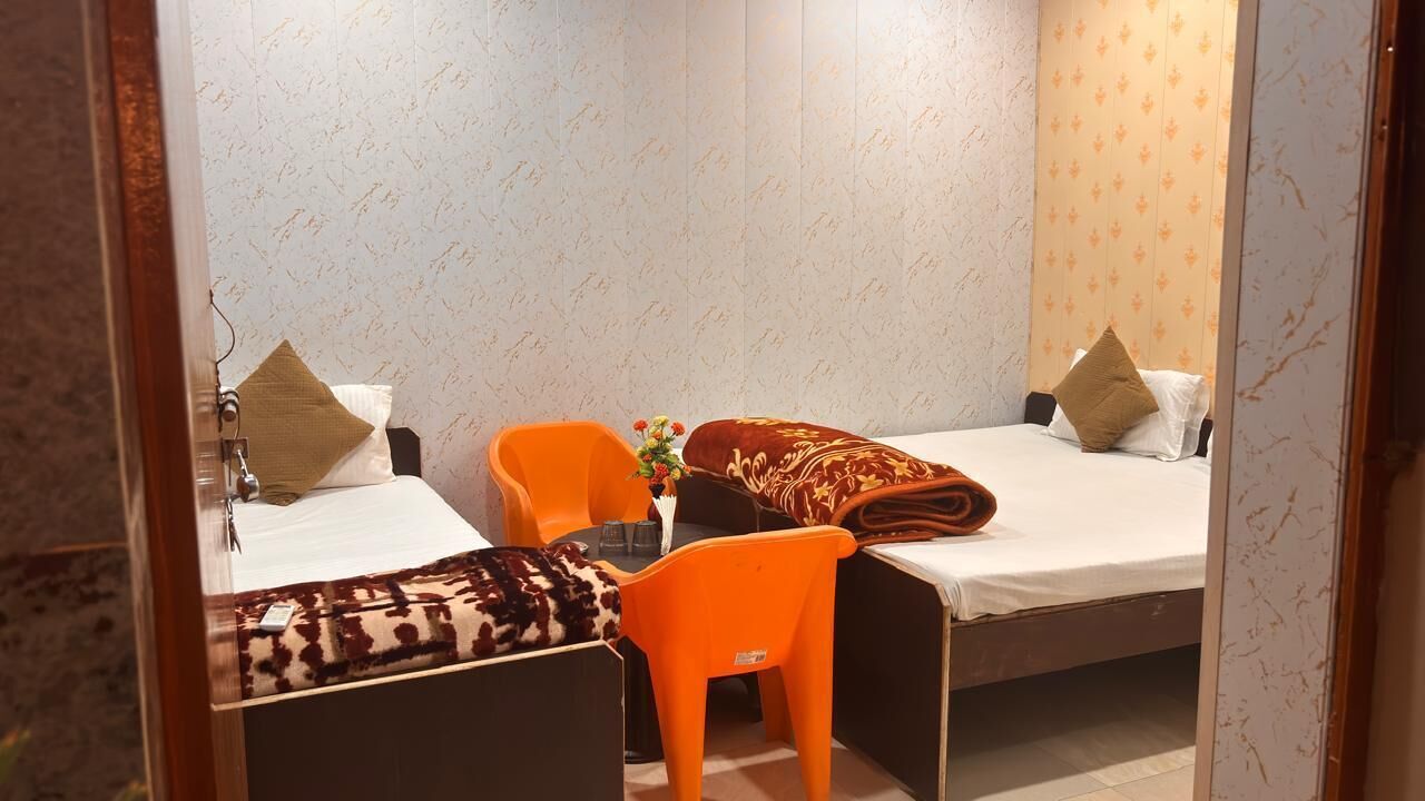 A small hotel room with two beds, a desk, and an orange chair.
