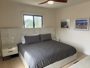 Un dormitorio con cama, mesita de noche y ventana con vista a la vegetación.
