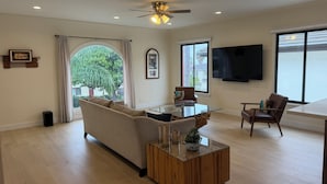 A spacious living room with a sofa, a glass coffee table, a ceiling fan, and a TV mounted on the wall. - Fully Renovated 2 BR House by Palos Verdes, Beach, in Quiet Neighborhood (Los Angeles)