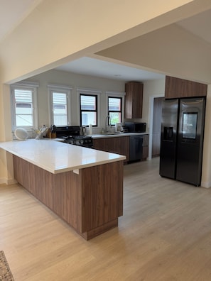 A modern kitchen with a central island, stainless steel appliances, and large windows.