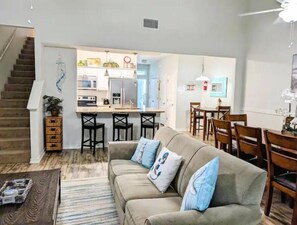 A living room with a sofa, coffee table, and a dining area with chairs and a table. - BEACH~HEATED POOL~PET FRIENDLY-WINTER STAY (Corpus Christi)