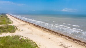 Une plage côtière avec une longue étendue de sable, quelques bâtiments dispersés et un ciel dégagé.