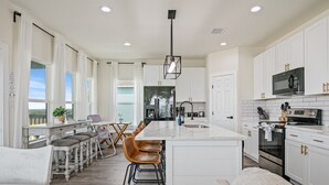 Une cuisine moderne avec des meubles blancs, un îlot central doté de tabourets, et un coin repas avec une table et des chaises.