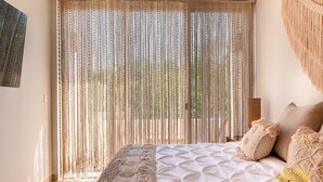 Un dormitorio con una cama grande, cortinas color crema y una manta tejida.