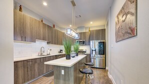 Una cocina moderna con armarios de madera, una isla central con taburetes altos, un microondas y un refrigerador de acero inoxidable.