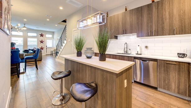 Una cocina moderna con armarios de madera, lavavajillas de acero inoxidable y una barra con taburetes.