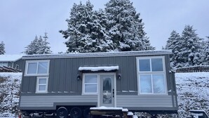 En grå mobilhome med veranda, en lille tilbygget garage, og et snedækket landskab.