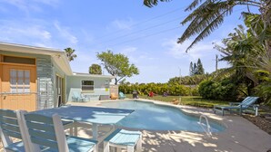 Ein Pool mit Liegestühlen und einem Tisch, umgeben von einem Garten und einem Haus.