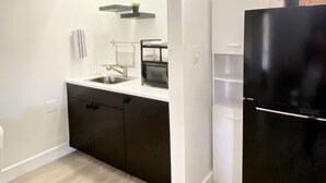 A modern kitchen with a black refrigerator, white cabinets, a microwave, and an air conditioning unit. - SouthWest Private Cozy Studio (Miami)