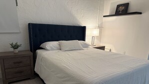 A neatly made bed with a dark headboard, a bedside table with a lamp, and a small plant on a wooden nightstand. - SouthWest Private Cozy Studio (Miami)