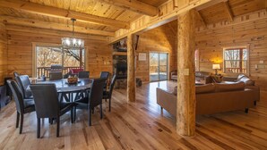 A log cabin interior with a dining area, fireplace, and a living room with a sofa. - Highland Lodge With Indoor Saltwater Pool (Rockbridge)