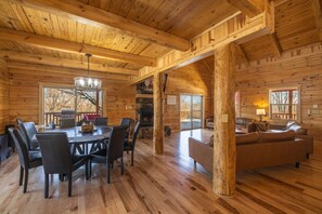 Interior de una cabaña de troncos con comedor, chimenea y sala de estar con sofá.