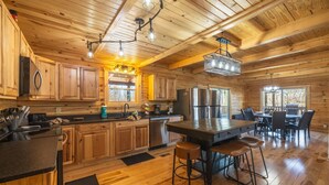 A spacious kitchen with wooden cabinets, a central island with stools, stainless steel appliances, and a dining area with a table and chairs. - Highland Lodge With Indoor Saltwater Pool (Rockbridge)