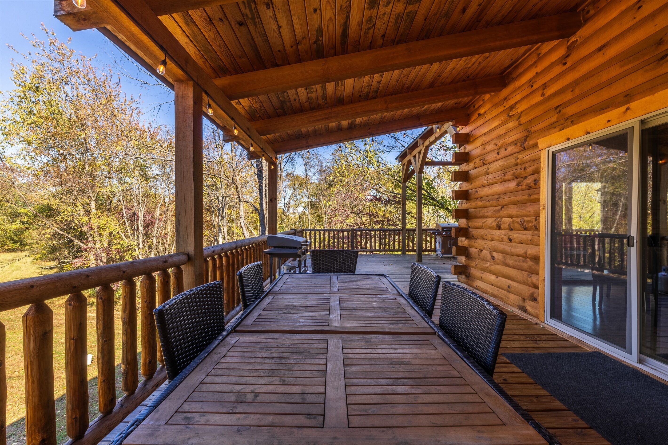 Une terrasse en bois dotée d’un espace salon couvert, d’un barbecue et offrant une vue sur les arbres environnants.