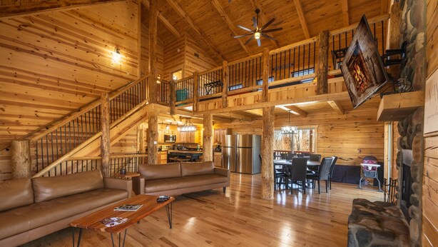 A spacious log cabin interior with a wooden staircase, a living room with a sofa and coffee table, a dining area, and a kitchen. - Highland Lodge With Indoor Saltwater Pool (Rockbridge)