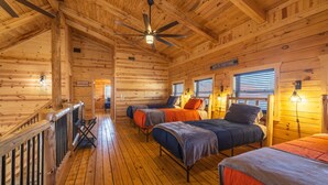 A log cabin interior with four beds, a wooden floor, a ceiling fan, and a sign that says 'NAILS FIX EVERYTHING.' - Highland Lodge With Indoor Saltwater Pool (Rockbridge)
